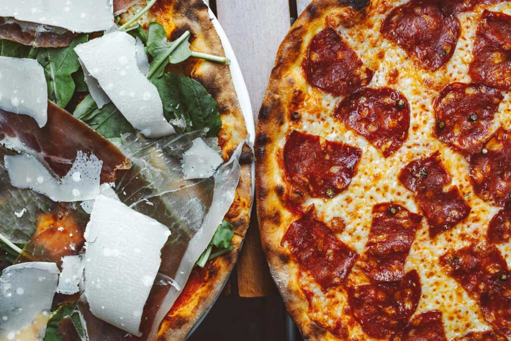 Two gourmet pizzas with mouth-watering toppings including pepperoni and prosciutto, perfect for food photography.